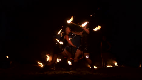 Slow-motion:-Professional-fire-performance-three-women-in-dripping-clothes-dance-and-spin-with-flaming-torches-and-a-man-with-flamethrowers-in-the-background.